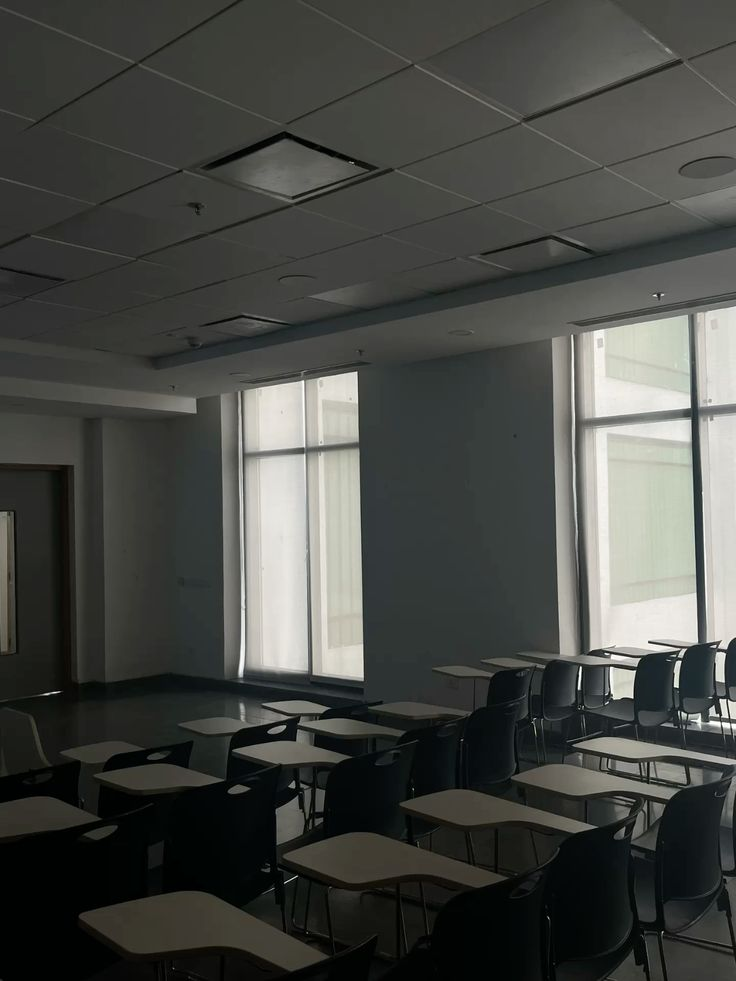 A shadowed lecture room with writing desks facing tall windows.
