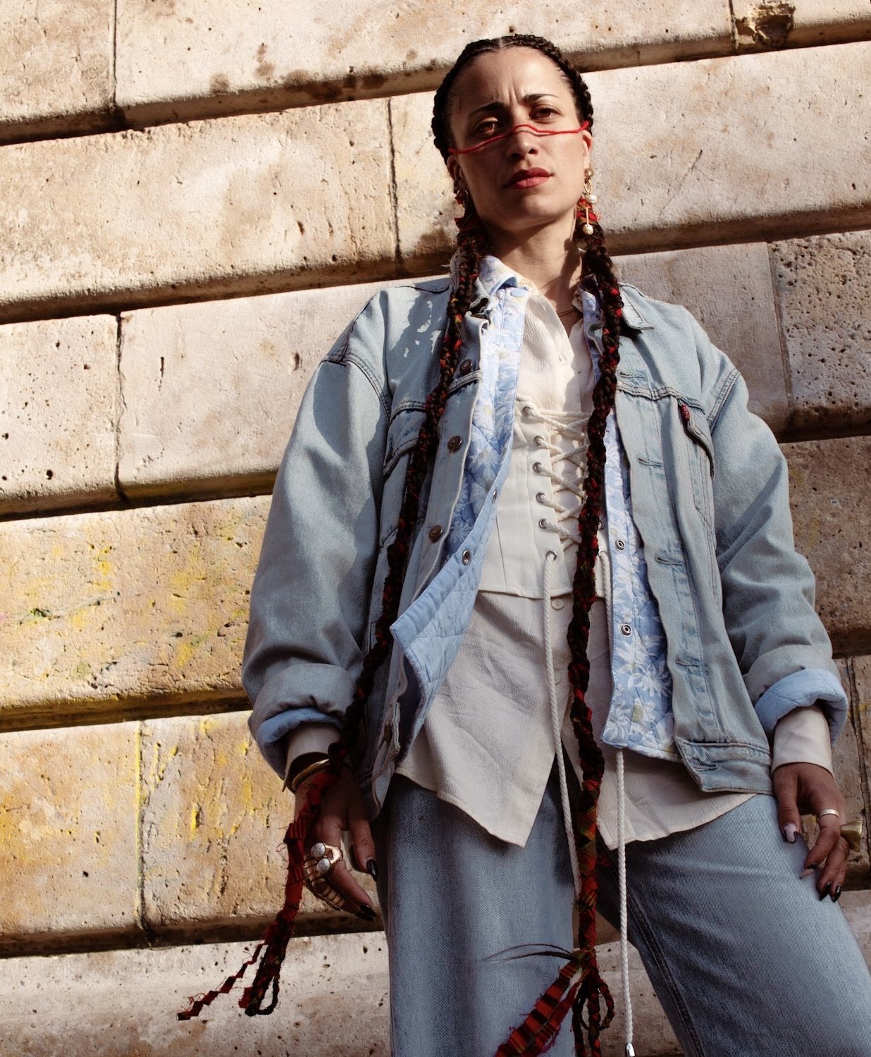 Portrait of Adriane Amri in red glasses and braided hair against stone steps.